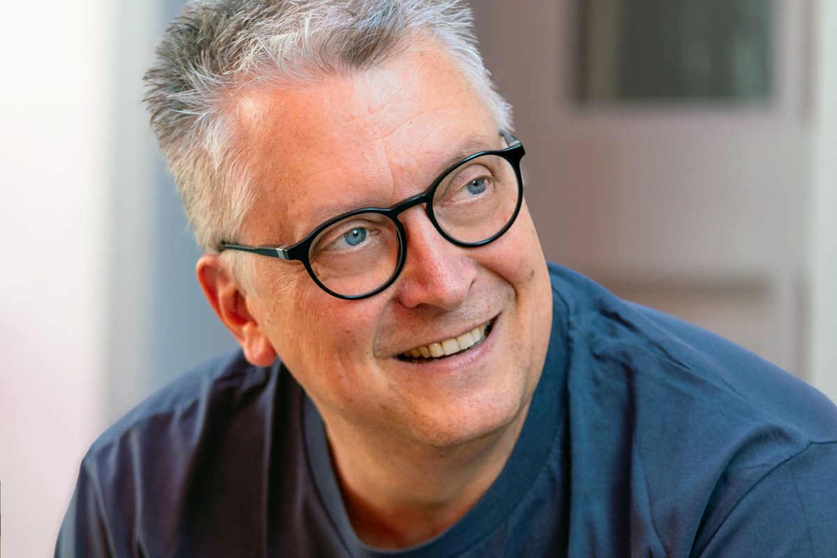 Jörg Hillemanns, Nahaufnahme: lächelnd, mit runder dunkler Brille, der Blick geht zur Seite